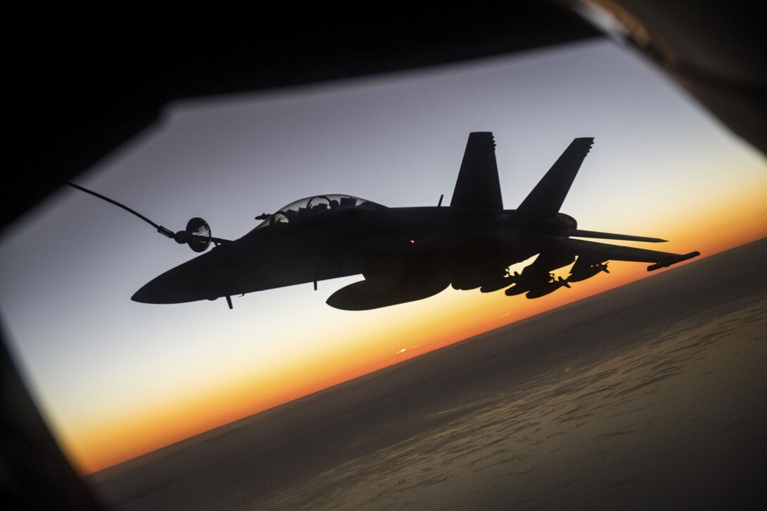 A fighter jet is framed by the horizon line underneath it, and the outlines of an aircraft from which it is receiving fuel.