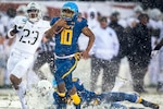 A man runs with a football through the snow.