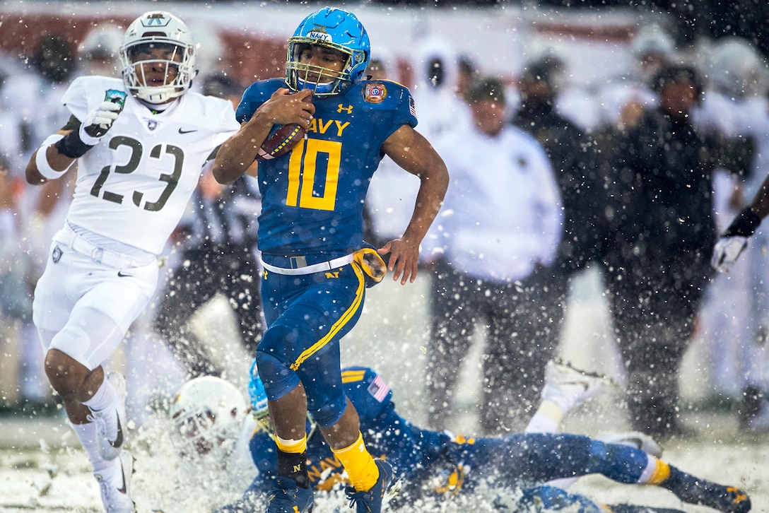 A man runs with a football through the snow.