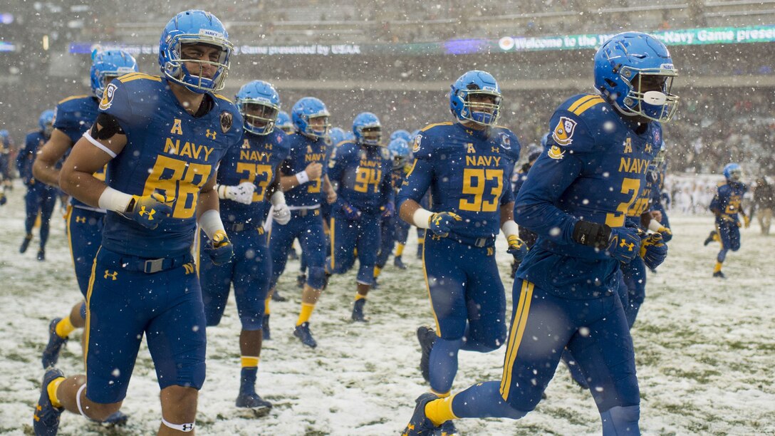 Football players run onto a snowy football field.