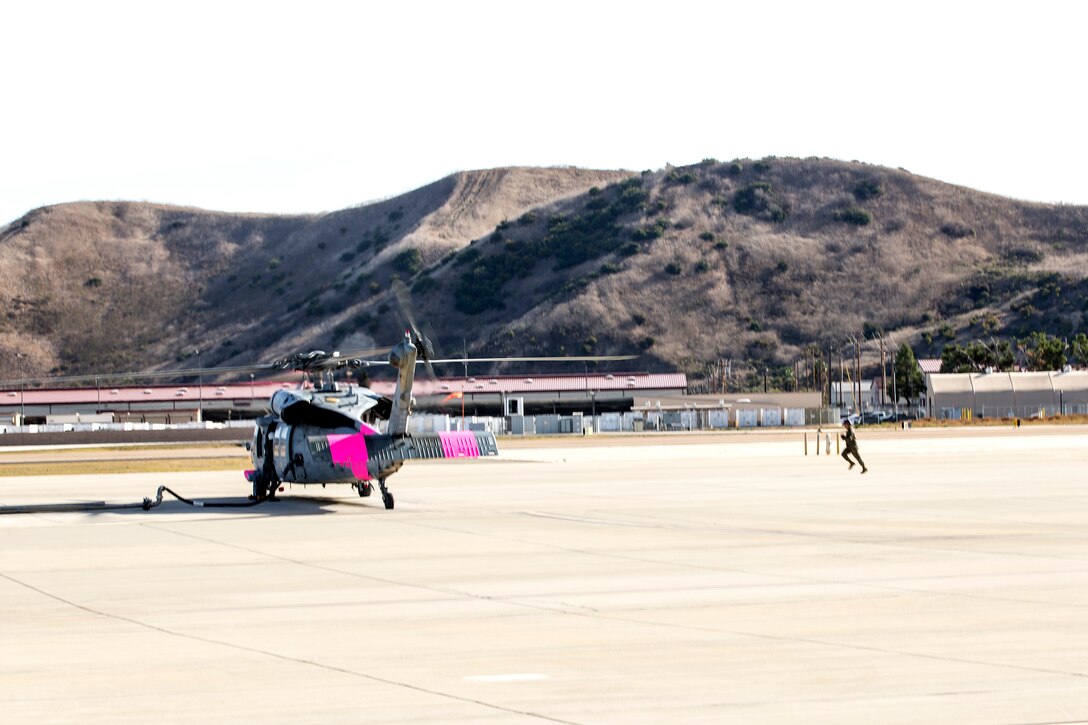 A helicopter sits on the ground with Marines moving around it.