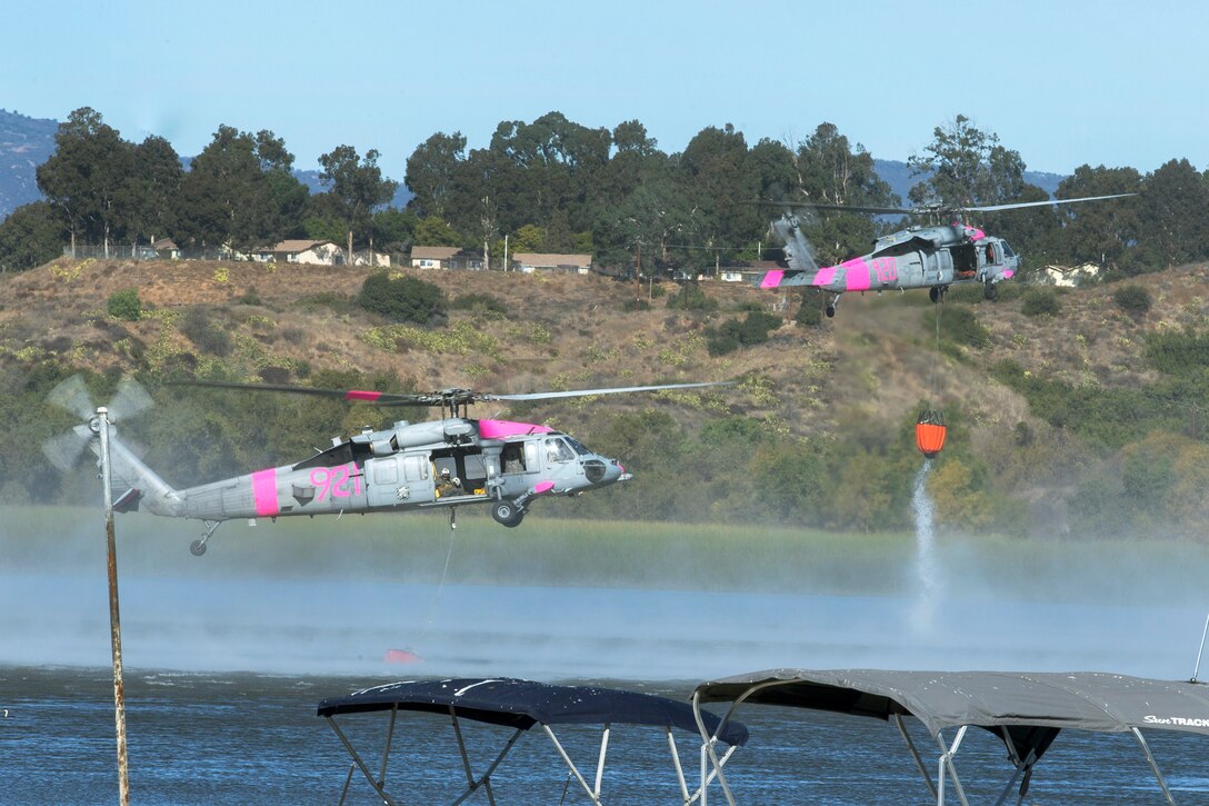 Two helicopters fly close to water.