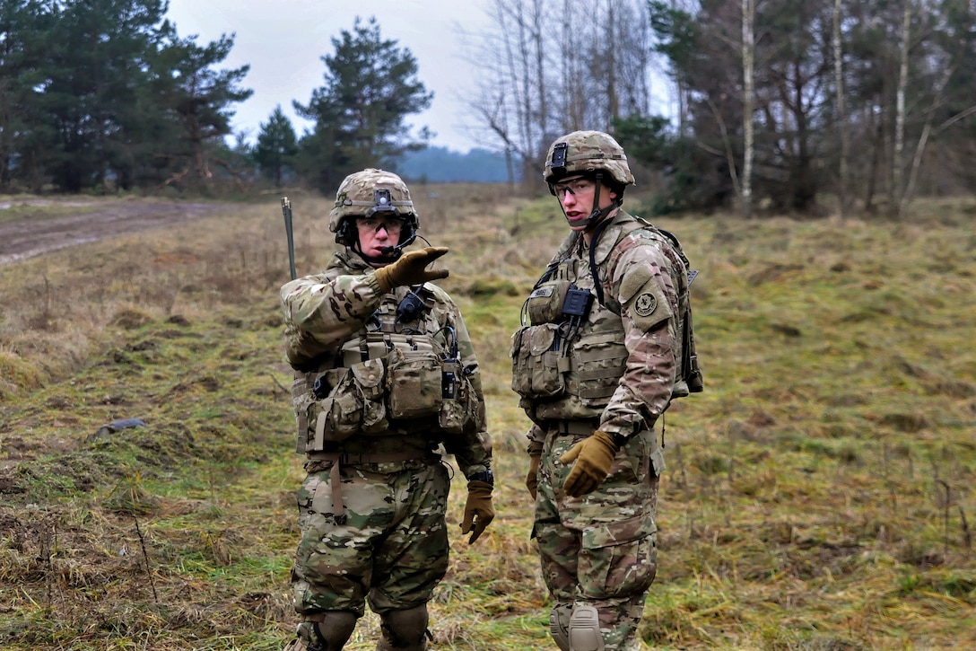 Two soldiers talk while standing in a field.