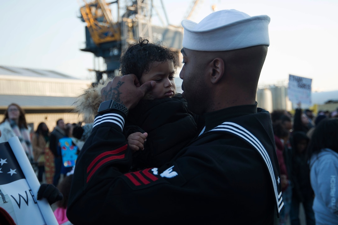 A sailor holds a small child.