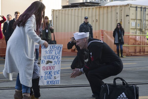 A sailor keels on the ground near a small child and a woman.