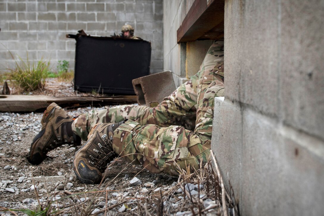 An airman crawls under a building during combat survival training.