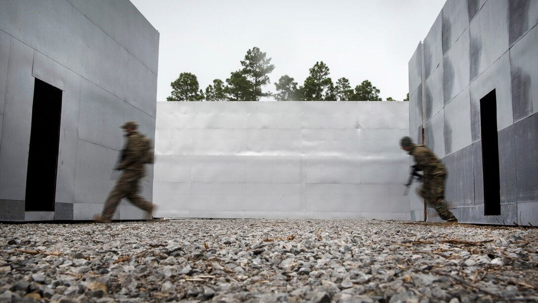 Air Force airmen evade opposing forces between buildings during combat survival training.
