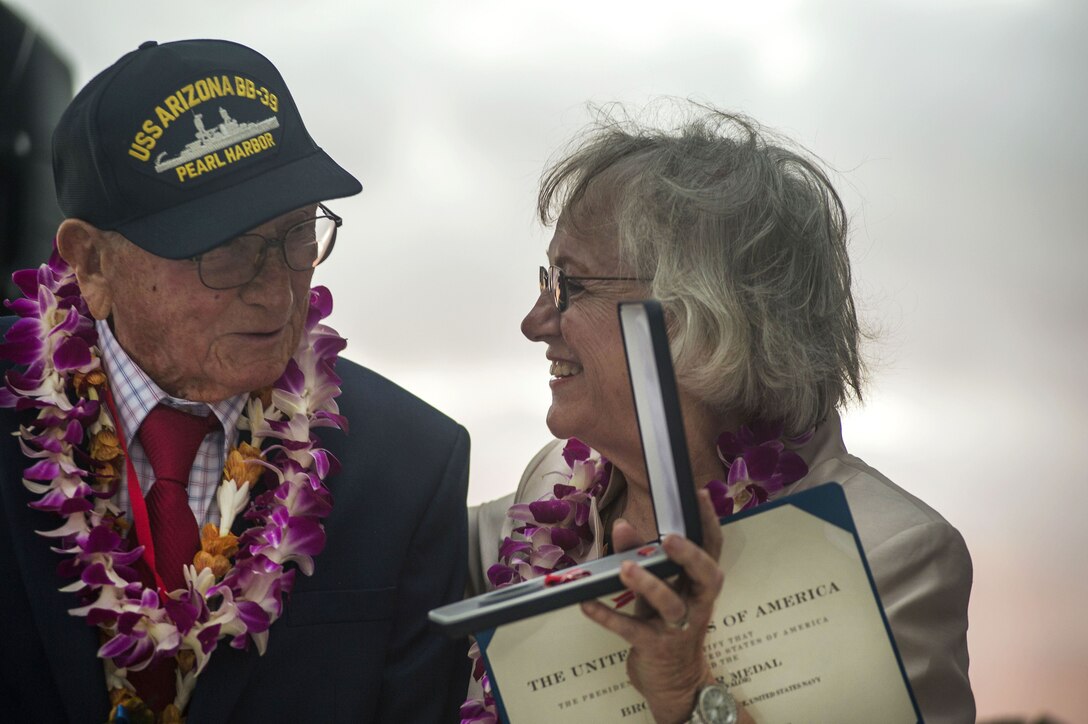 A woman holds a medal for a veteran to see.