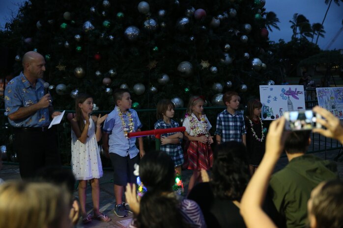 Mr. Doug Wadsworth, chief of staff, Marine Corps Base Hawaii (MCBH), calls forward the winners of the Mokapu Elementary’s art, paragraph and essay contest during the Annual Tree Lighting Ceremony held aboard MCBH, Nov. 30, 2017. Mr. Doug Wadsworth lit the tree with the help of the winners of Mokapu Elementary’s art, paragraph and essay contest. (Marine Corps Photo by Sgt. Alex Kouns/Released)