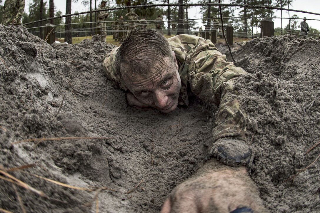 An airman crawling on wet sand under wire reaches one arm forward.