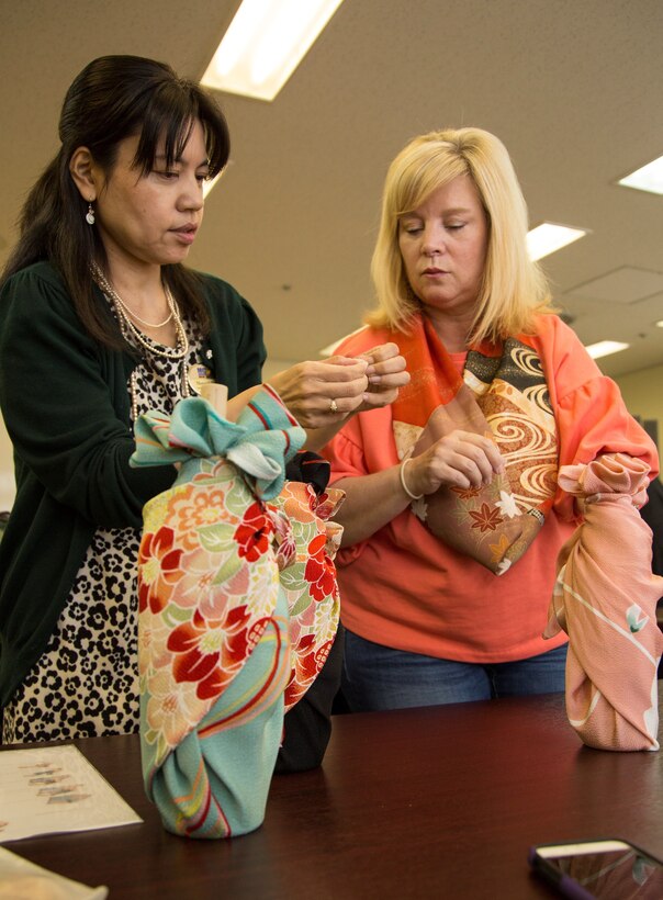 CAMP FOSTER, OKINAWA, Japan- Megumi Tamaki, left, shows Melinda Blakley, how to wrap glass bottles during a Furoshiki gift wrapping class Nov. 21 at the Family Readiness Center aboard Camp Foster, Okinawa, Japan.