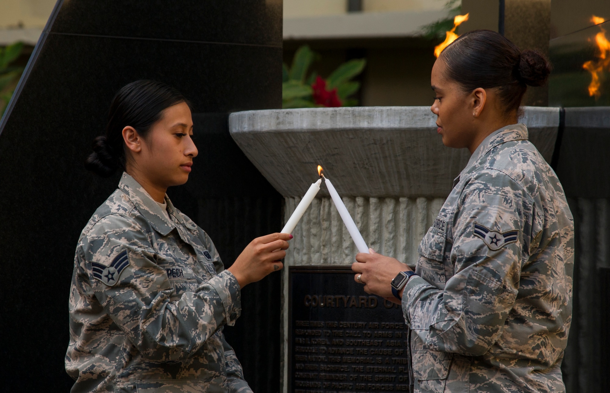 U.S. Air Force Senior Airman Summer Pech, Pacific Air Forces personnelist, passes a flame to Airman 1st Class Racheli Velez, Pacific Air Forces personnelist, during a remembrance ceremony for U.S. Army Air Corps Pfc. Joseph Nelles at the Courtyard of Heroes in the Pacific Air Forces headquarters building, Joint Base Pearl Harbor-Hickam, Hawaii, Dec. 10, 2017.  Nelles, a chaplain’s assistant, was killed during the 1941 attack on Hickam Field.  (U.S. Air Force photo by Tech. Sgt. Heather Redman)