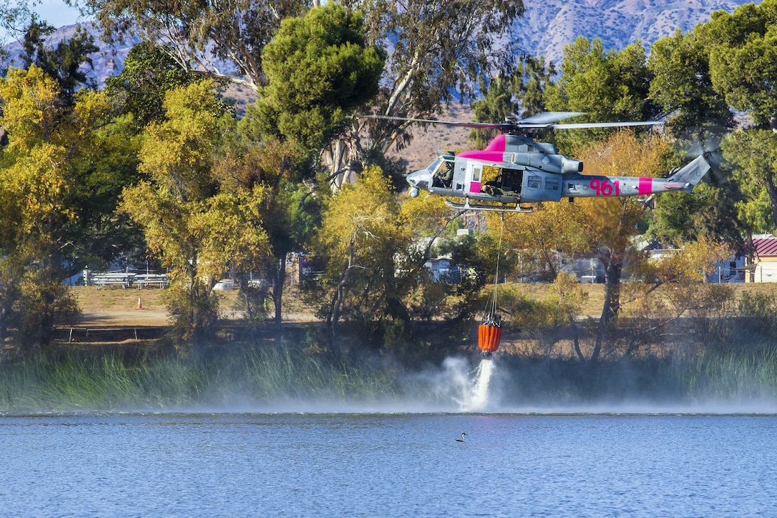 A helicopter fills an orange bucket with water from a lake.