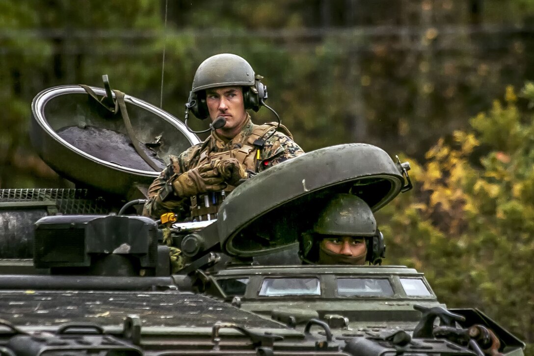 Two Marines look out from the top of a tank.