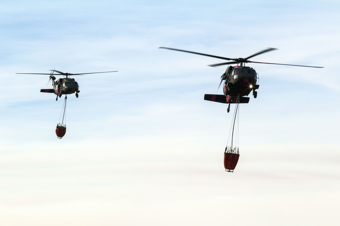 Two Army helicopters carrying buckets land to refuel .
