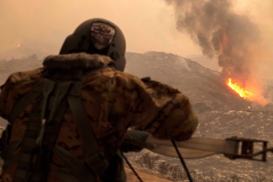 A soldier watches a wildfire from a helicopter.
