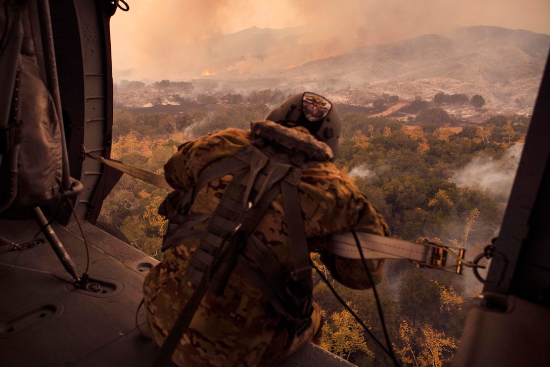 A soldier watches a wildfire from a helicopter.