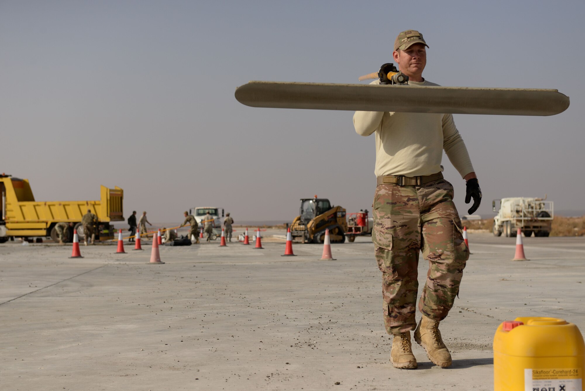 Staff Sgt. Joshua Swertfager, a native of Fresno, Calif., assigned to the 332nd Expeditionary Civil Engineer Squadron carries a large squeegee to another location after smoothing out a new concrete slab on the runway of an undisclosed location in Southwest Asia Nov. 28, 2017. Swertfager, a heavy equipment operator worked with other squadron members to repair a runway due to wear and tear of constant use by U.S. and Coalition forces flying sorties against ISIS. (U.S. Air Force photo by Senior Master Sgt. Cohen A. Young)