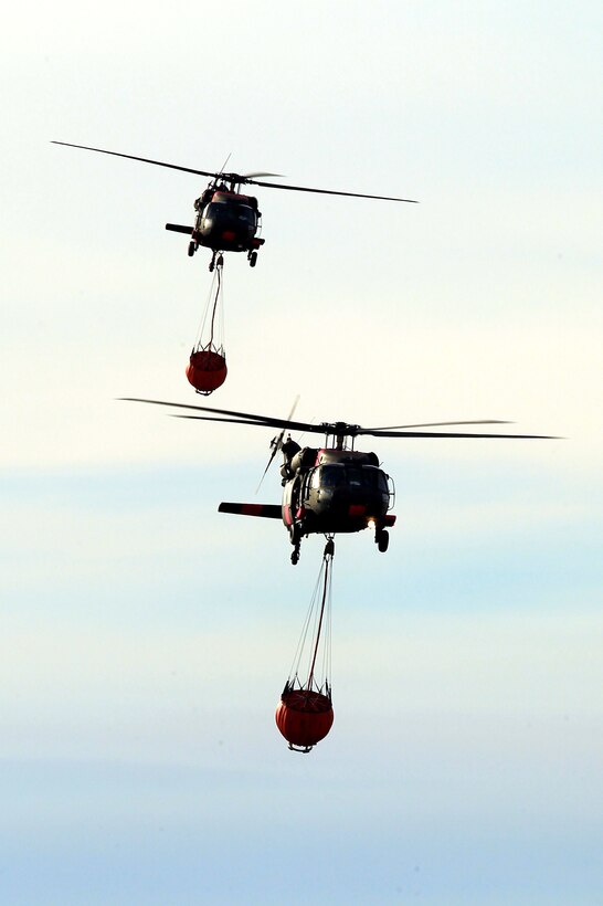 Two UH-60 Black Hawk helicopters transport water buckets during firefighting efforts