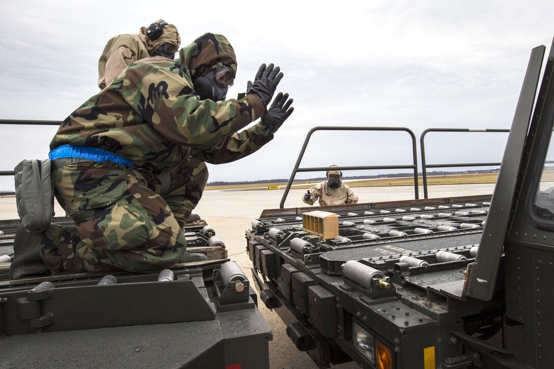 An airman wearing mission oriented protective posture level two gear indicates the distance to a K-loader driver.