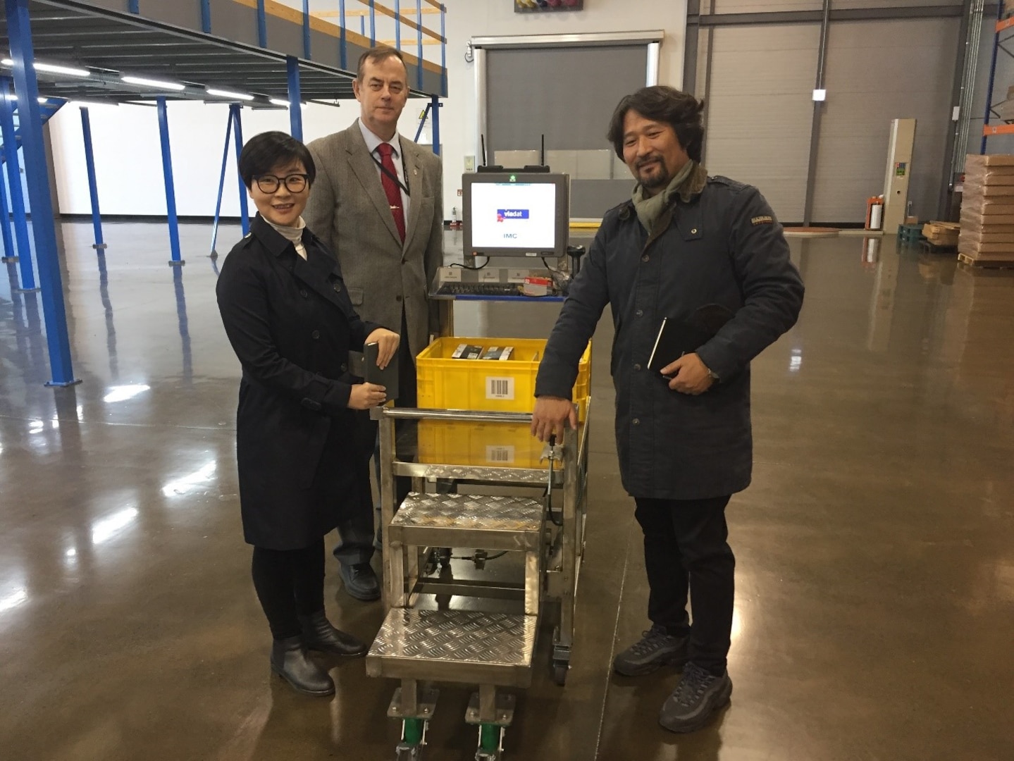 O, Hyon Yong, Dave Harris, and Kim, Yong Ki examining the Taegu Tec mobile cart. The cart is light weight, easily manuverable, has an inexpensive power supply and a built-in step ladder to work in the under mezzine walk and pick area.