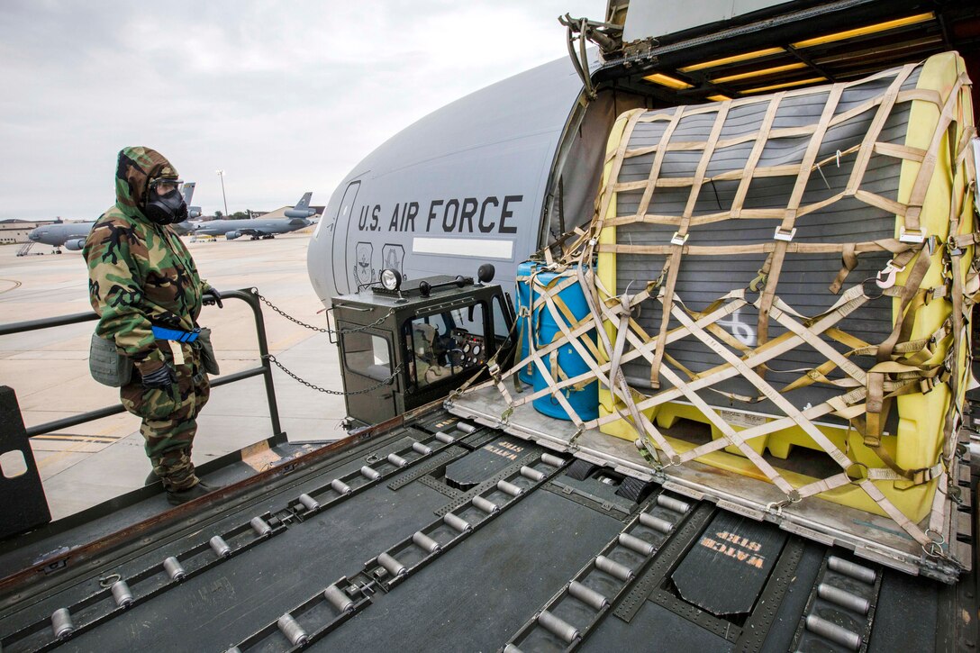 An airman wearing mission oriented protective posture level two gear directs the off-loading of cargo.