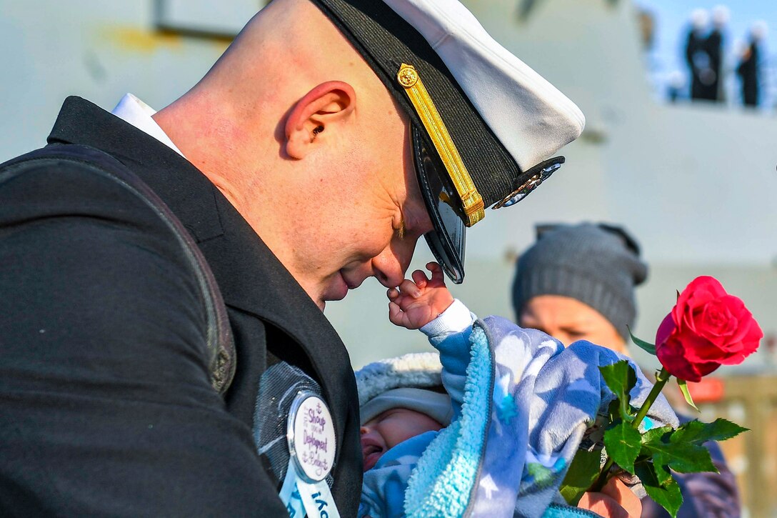A smiling sailor bows his head with eyes closed as a baby he's holding touches his nose.