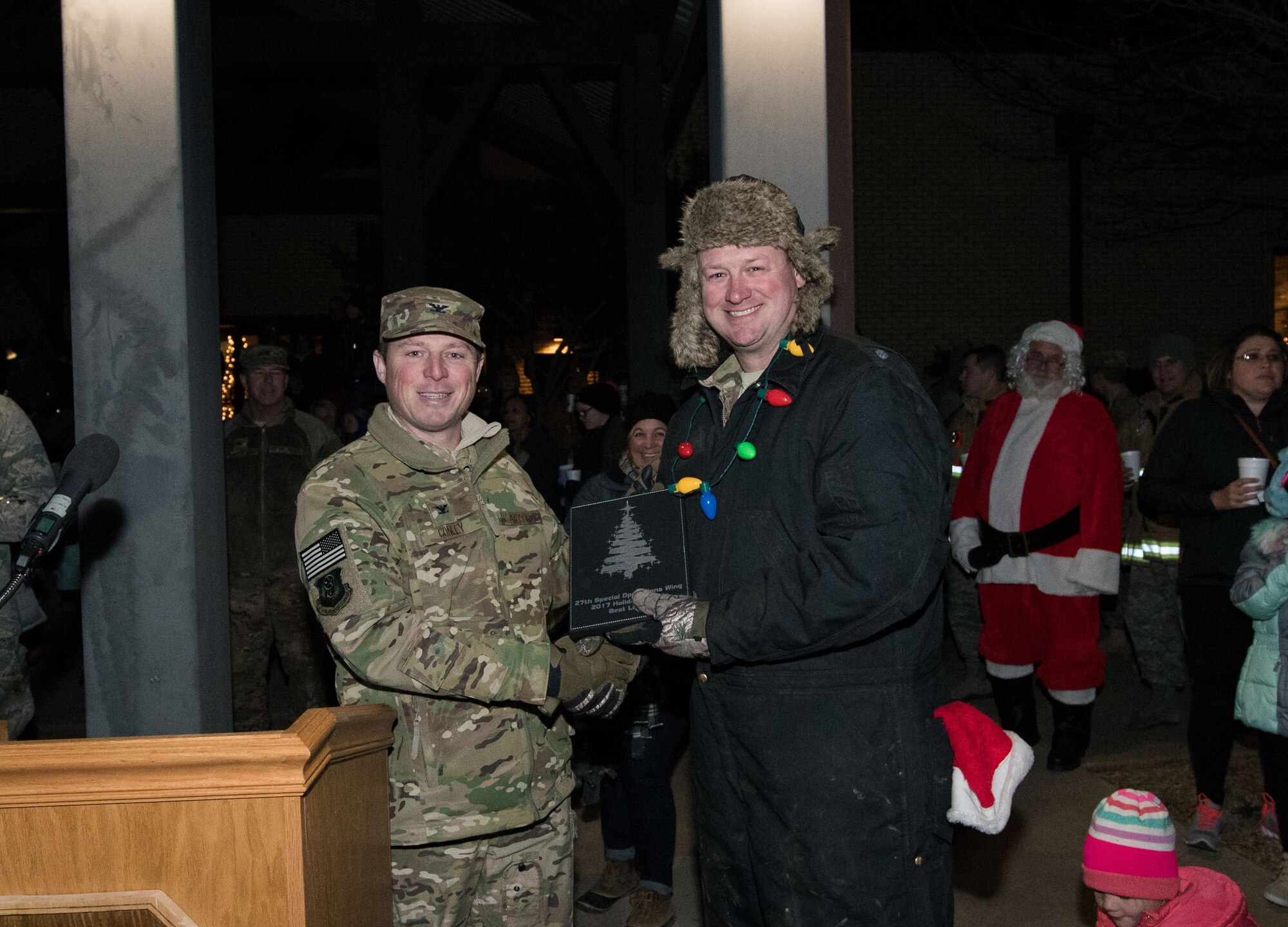 Col. Michael Conley, 27th Special Operations Wing vice commander, presents a member of the 27th Special Operations Maintenance Squadron an award for best light display during the holiday parade and tree lighting ceremony Dec. 7, 2017, at Cannon Air Force Base, New Mexico. Conley handed out awards for best light display, most spirited float and best overall float. (U.S. Air Force photo by Staff Sgt. Michael Washburn/Released)