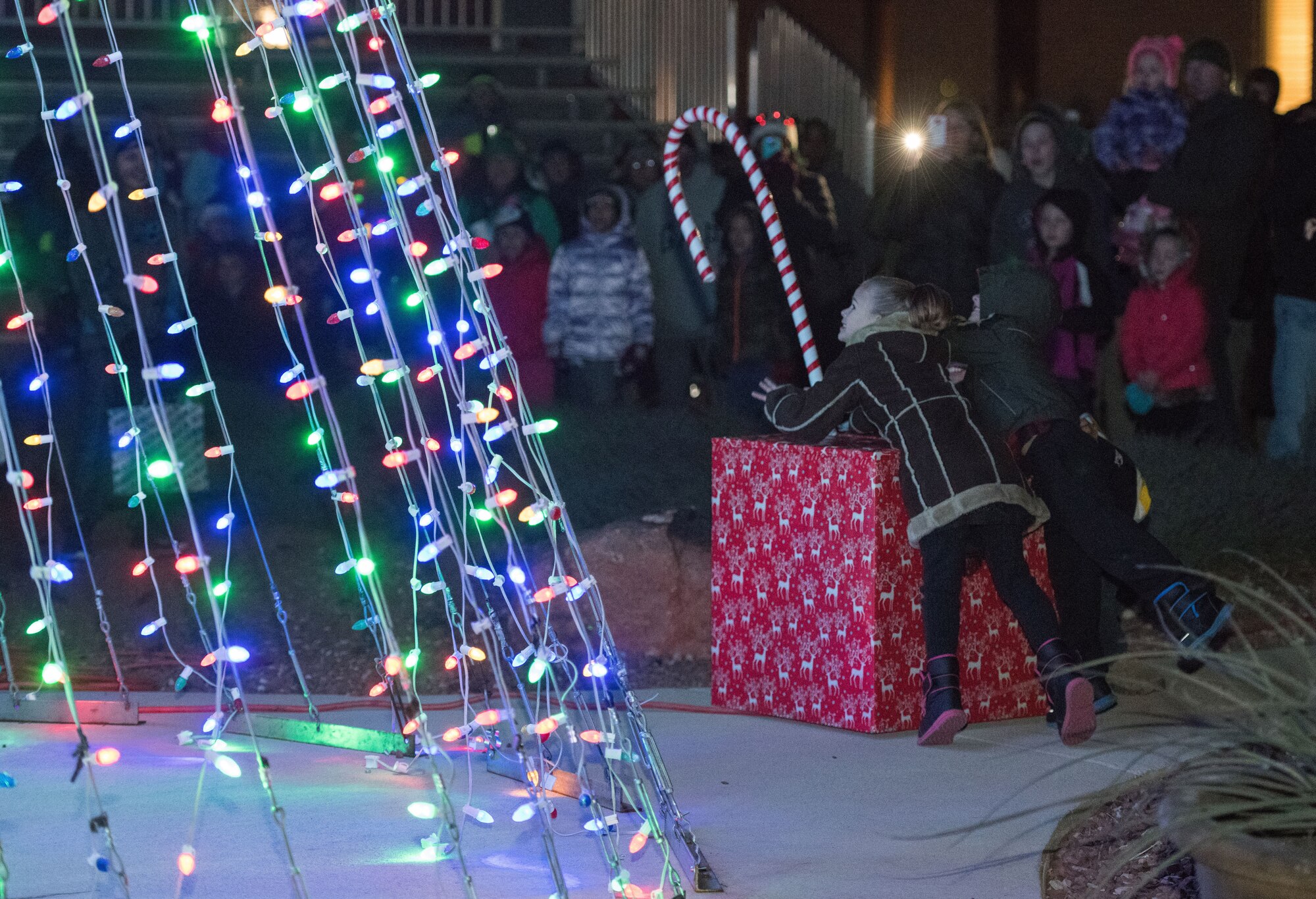 Bailey and Taytim Jones flip a candy cane rigged to holiday lights during the holiday parade and tree lighting ceremony Dec. 7, 2017, at Cannon Air Force Base, New Mexico. The parade included floats decorated by the squadrons and an appearance by Santa Claus himself. (U.S. Air Force photo by Staff Sgt. Michael Washburn/Released)