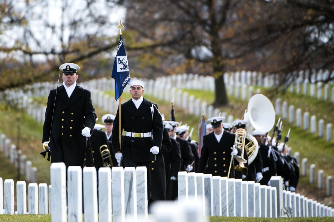 Sailors walk in formation through rows of white headstones.