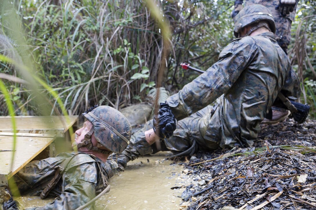 A Marine helps pull a team member out of the swampy waters while participating in an endurance course.