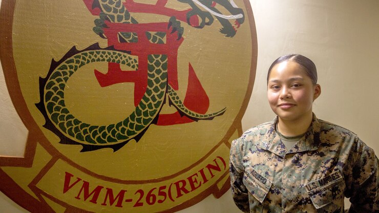 A Marine poses next to an emblem on the wall.