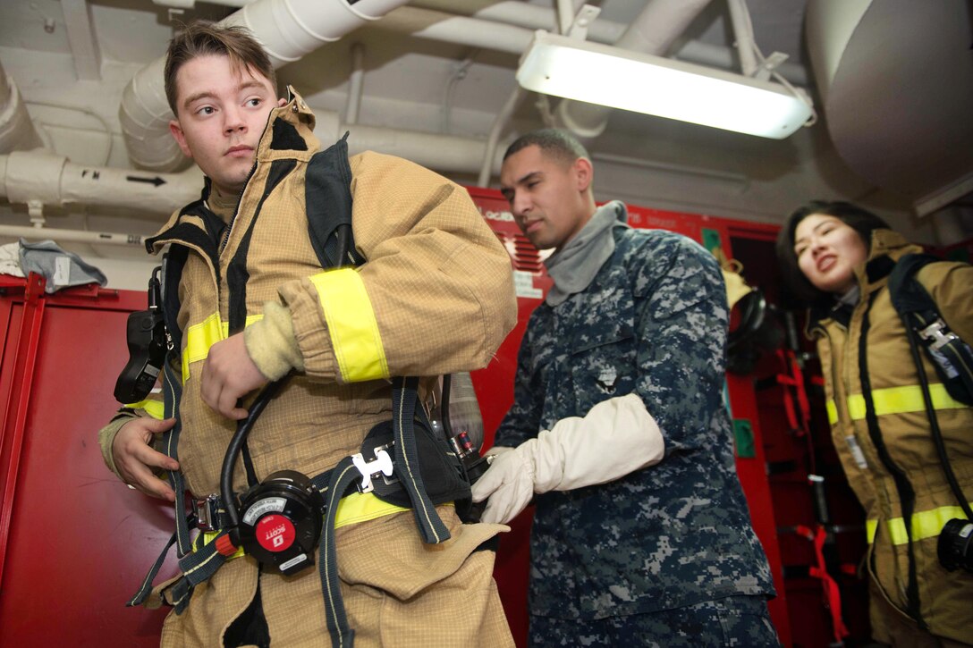 Navy Petty Officer 3rd Class Kevin Calvert dons a fire fighting gear before participating in a general quarters drill.