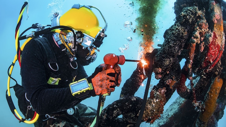 A cuts uses a tool with a flame to cut a section of metal underwater.