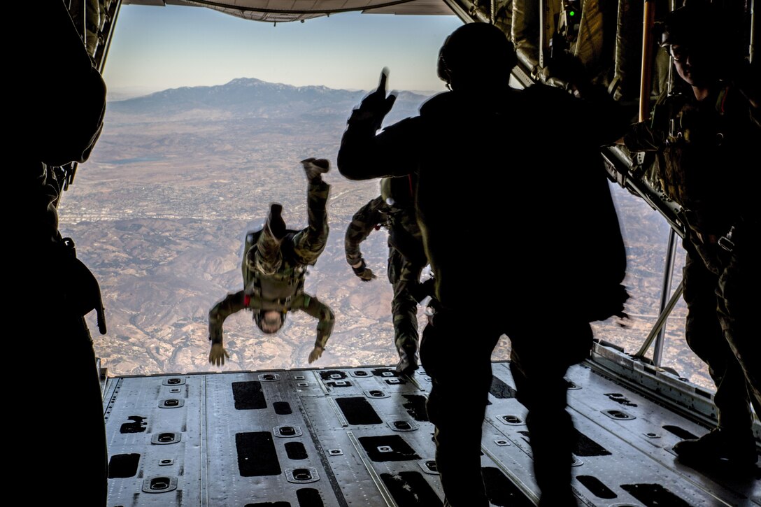 A Marine jumps out of the back of an aircraft, as two others prepare to do the same.