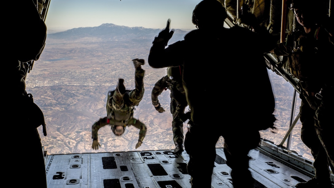 A Marine jumps out of the back of an aircraft, as two others prepare to do the same.