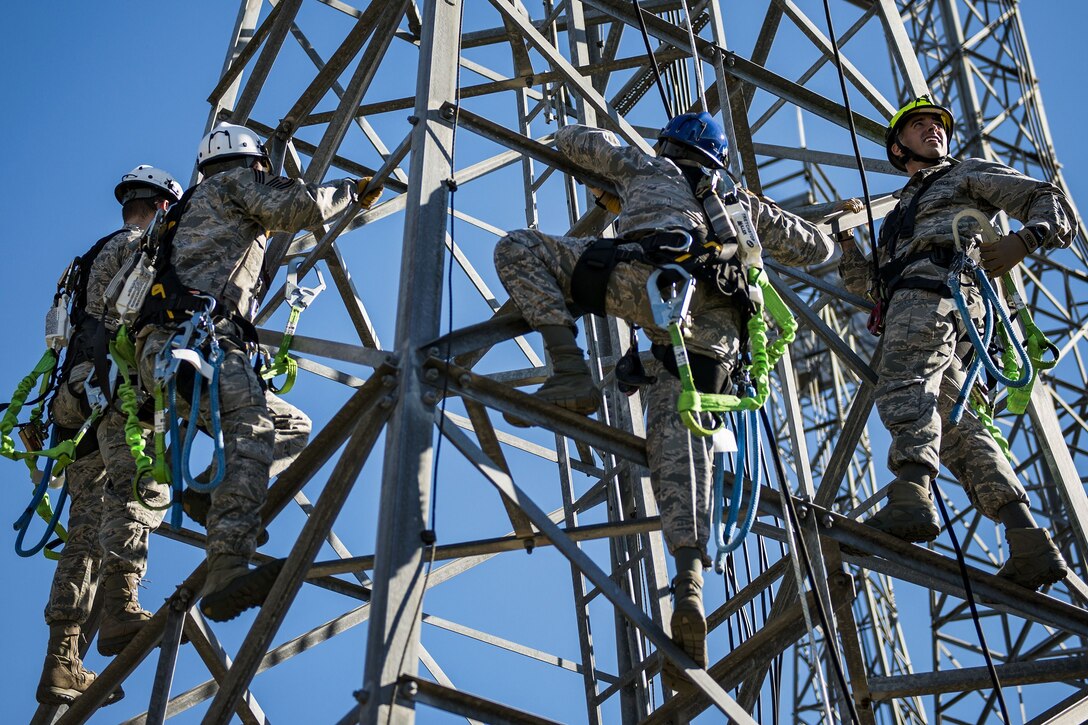 Several airmen with climbing gear stand on a tower.