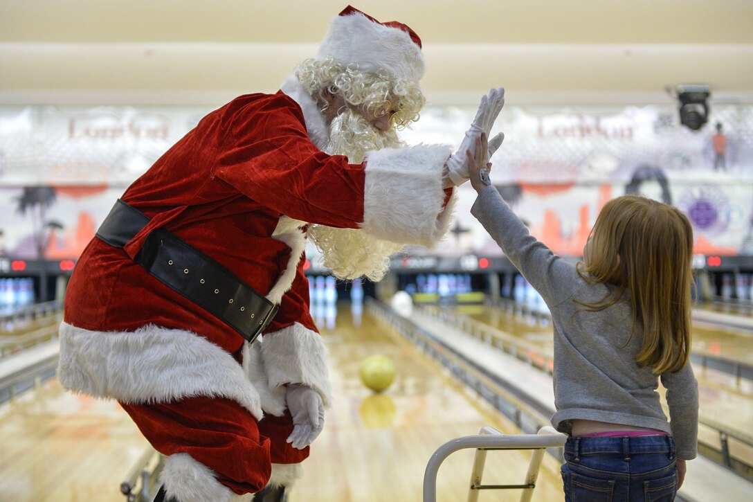 A man dressed as Santa Claus high-fives a girl in a bowling alley.