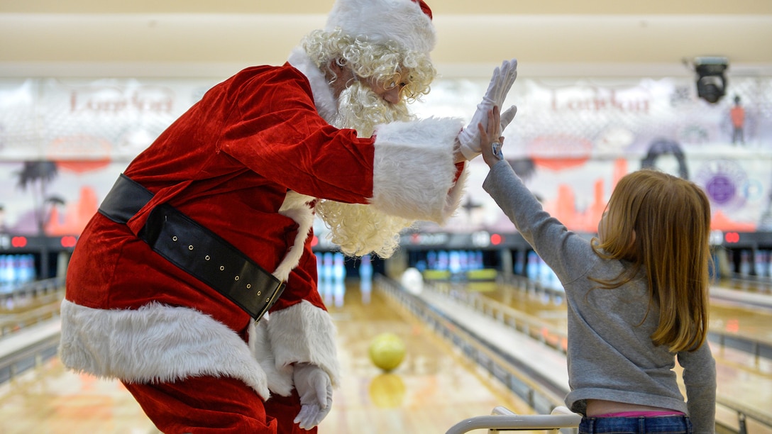 A man dressed as Santa Claus high-fives a girl in a bowling alley.