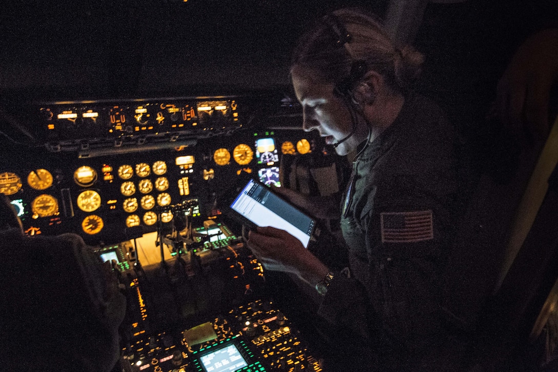 A pilot in a dark cockpit with uillum looks at a screen.