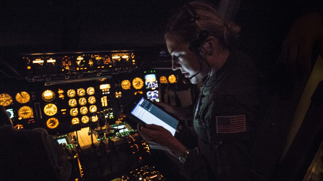 A pilot in a dark cockpit with uillum looks at a screen.