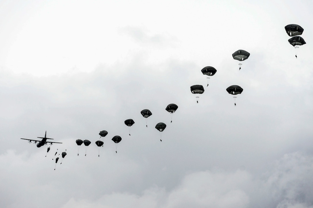 Paratroopers jump from an aircraft during overcast conditions.