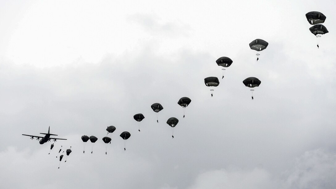 Paratroopers jump from an aircraft during overcast conditions.