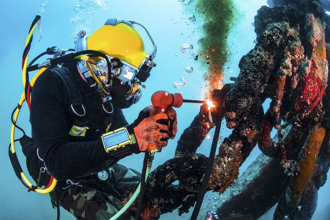 A cuts uses a tool with a flame to cut a section of metal underwater.