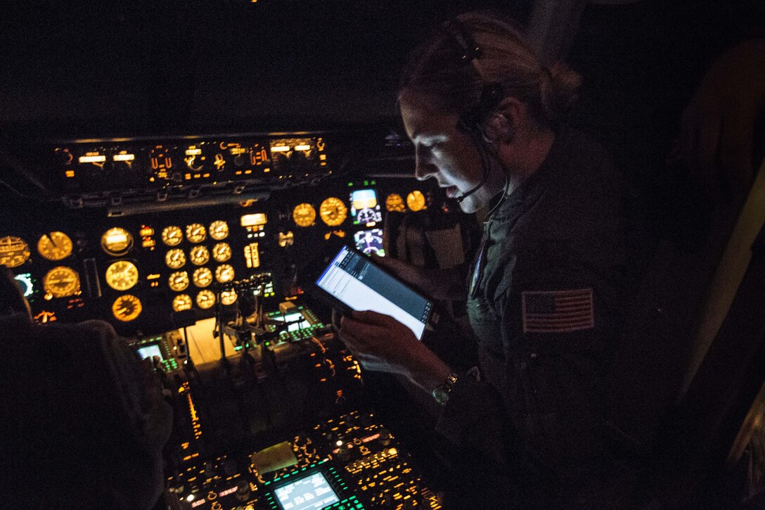 A pilot in a dark cockpit with uillum looks at a screen.