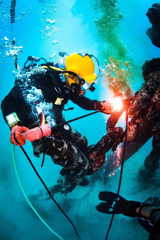 A Navy diver uses an underwater torch to cut an object.