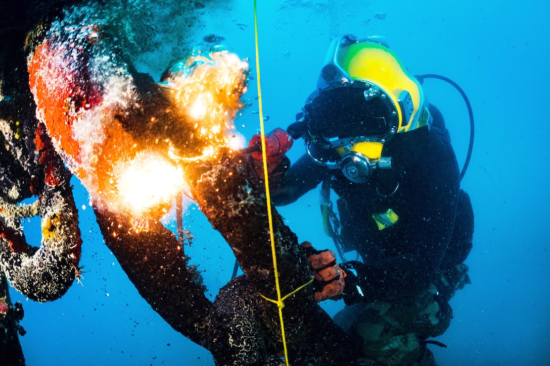 A diver uses a cutting torch underwater.