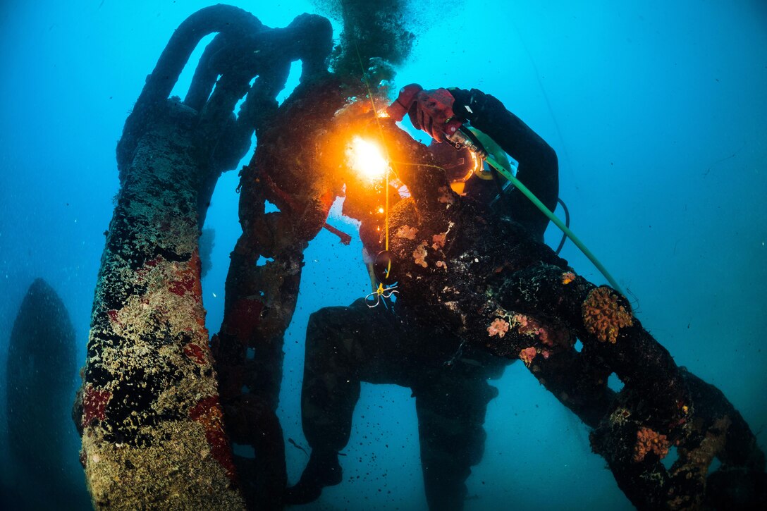 A diver uses an underwater torch to cut an object.