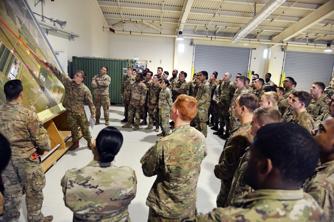 Soldiers gather around another solider speaking.