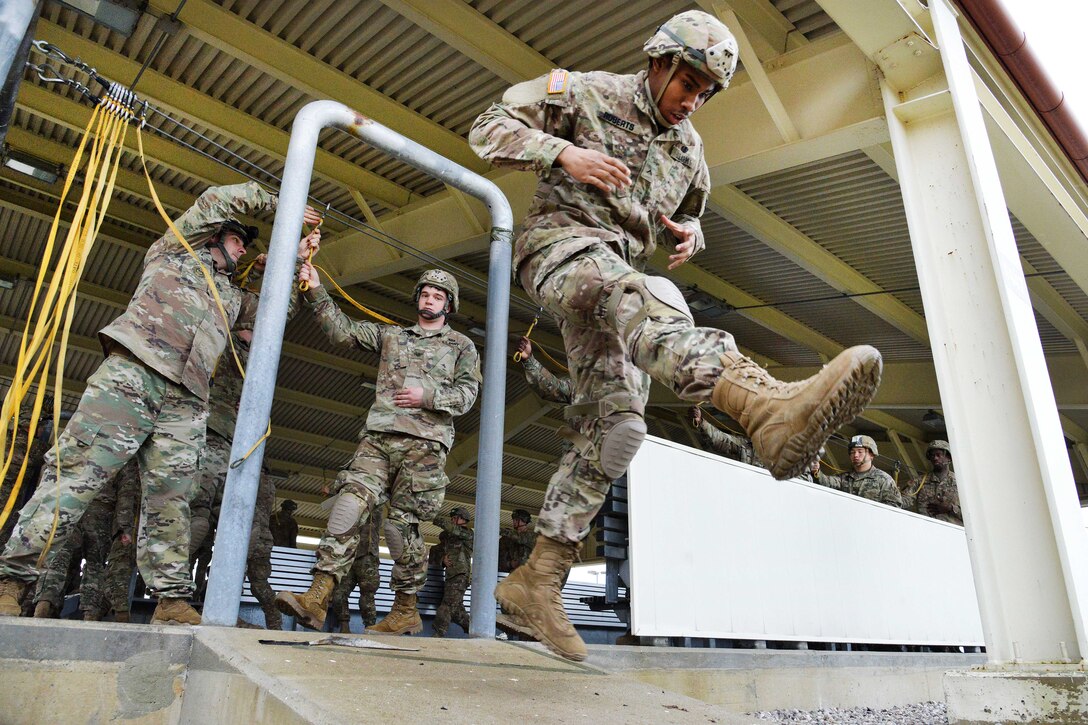 Soldiers step off a ledge onto the ground.